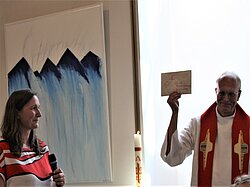 Ein Priester hält ein religiöses Objekt, eine Frau steht links.