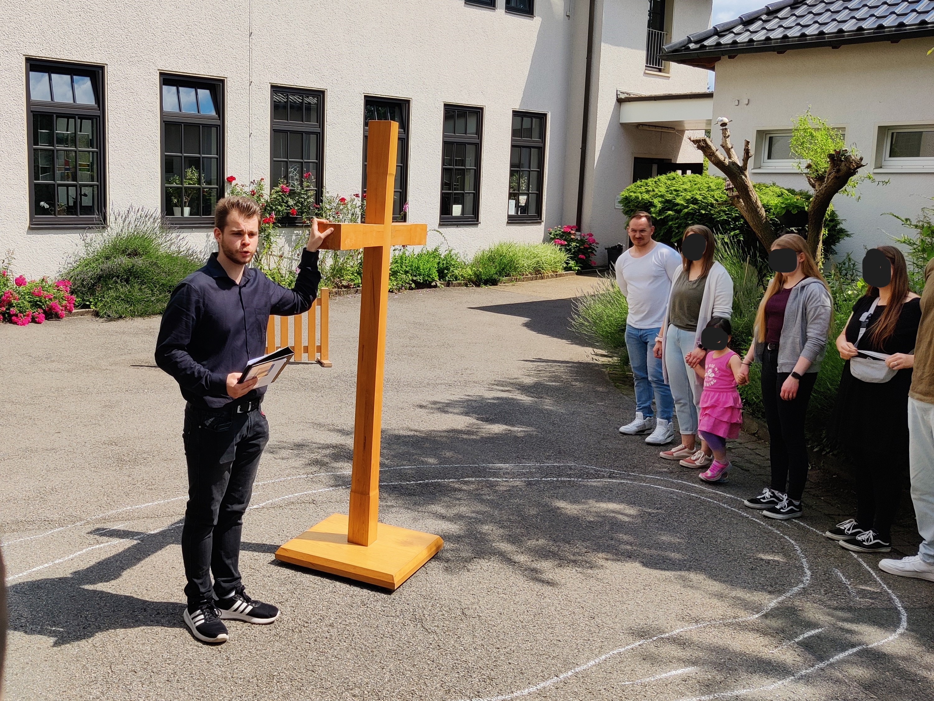 Mann präsentiert einer Gruppe von Menschen im Freien ein großes Holzkreuz.