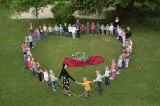 Kinder bilden eine Herzform auf einer Wiese.