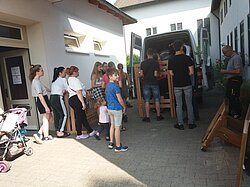 ugendliche und Erwachsene laden Gegenstände in einen Lieferwagen auf einem Hof.