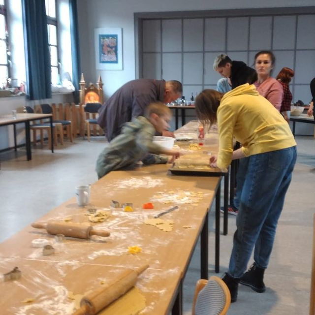 Personen beim Teig ausrollen und Plätzchen backen an einem langen Tisch.
