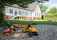 Sandkasten mit Spielzeug-Baufahrzeugen vor einem Gebäude.