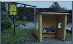 Miniatur-gelbe Bushaltestelle mit Rucksäcken und einem Bushaltestellenschild.
