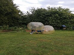Zwei Personen in aufblasbaren Bällen spielen auf einer Wiese.