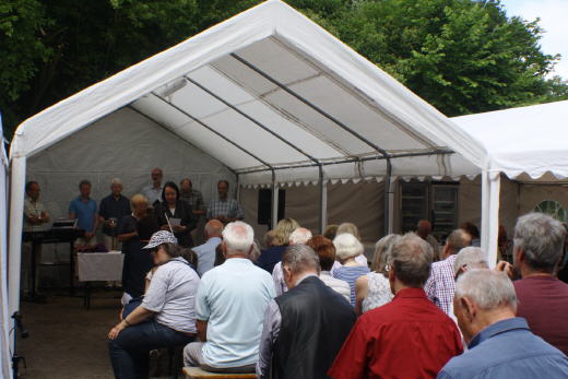 Menschen unter einem weißen Zelt im Freien versammelt.