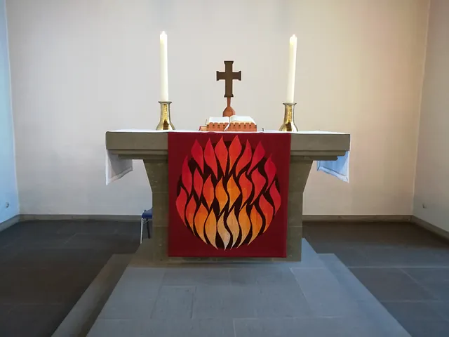 Altar mit rotem Tuch mit Flammendesign, Kerzen und Kreuz.