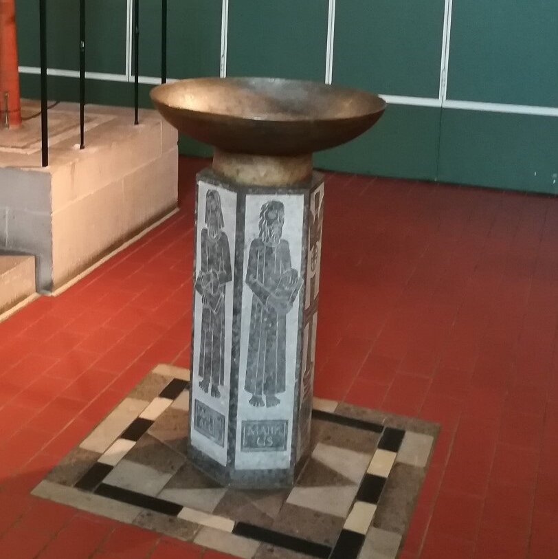 Ein Taufbecken auf einer Granitstele mit geschnitzten Figuren und einem Taufbecken aus Kupfer.