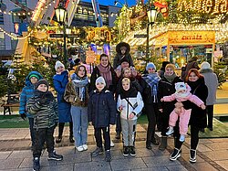 Eine Gruppe Leute, darunter Kinder und Erwachsene, steht auf einem Weihnachtsmarkt.