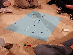 Füße um ein Bodenbrettspiel mit einem blauen Tuch und Spielsteinen.