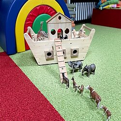 Hölzernes Noahs Arche-Spielzeug mit Tierfiguren auf grünem und rotem Teppich.