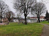 Grünfläche im Freien mit Gebäuden und kahlen Bäumen.