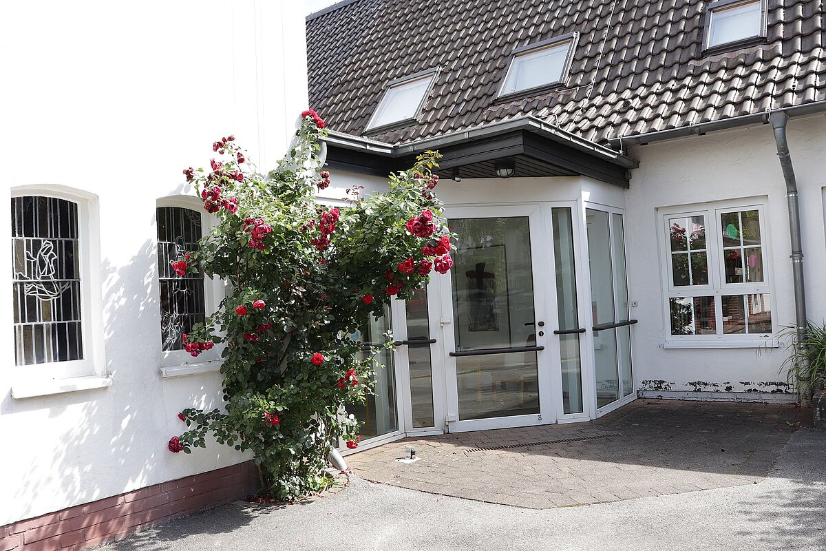 Eingang eines weißen Gebäudes, bewachsen mit roten Kletterrosen.