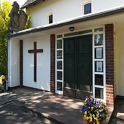 Eingangsbereich einer weißen Kirche mit einem braunen Kreuz