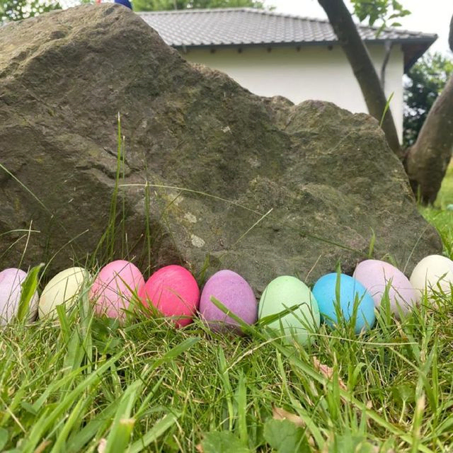 Bunte Eier im Gras vor einem Stein.