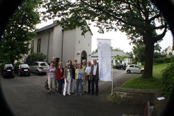 Gruppe von Personen steht vor einer Kirche mit Fahne.