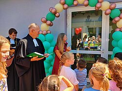 Geistlicher spricht zu Kindern bei einer Veranstaltung mit Luftballons.