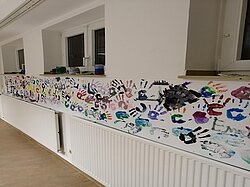 Eine Wand ist mit bunten Handabdrücken und Kunstwerken geschmückt.